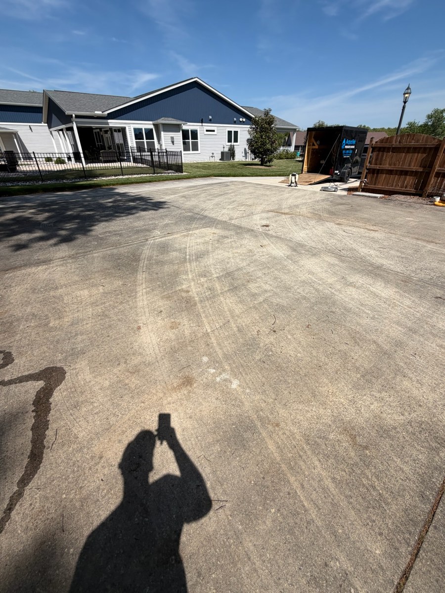 Concrete apron at a townhome building before washing, dark traffic marks worked into the slab