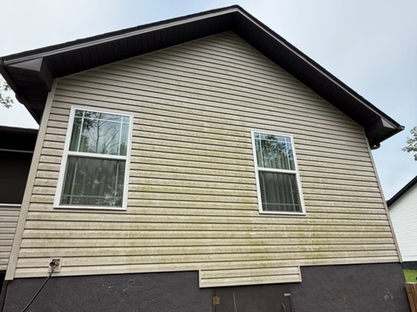 Gable end of a house before soft washing, the vinyl siding stained green with algae