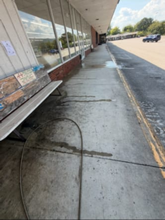 Commercial storefront sidewalk before washing, dark traffic grime worked into the concrete