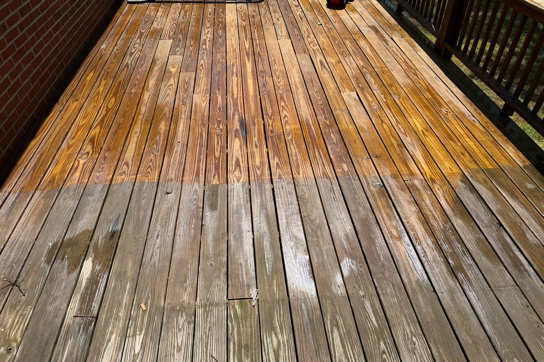 A wood deck halfway through a wash, the cleaned boards back to a warm golden grain against the grey weathered half still to do